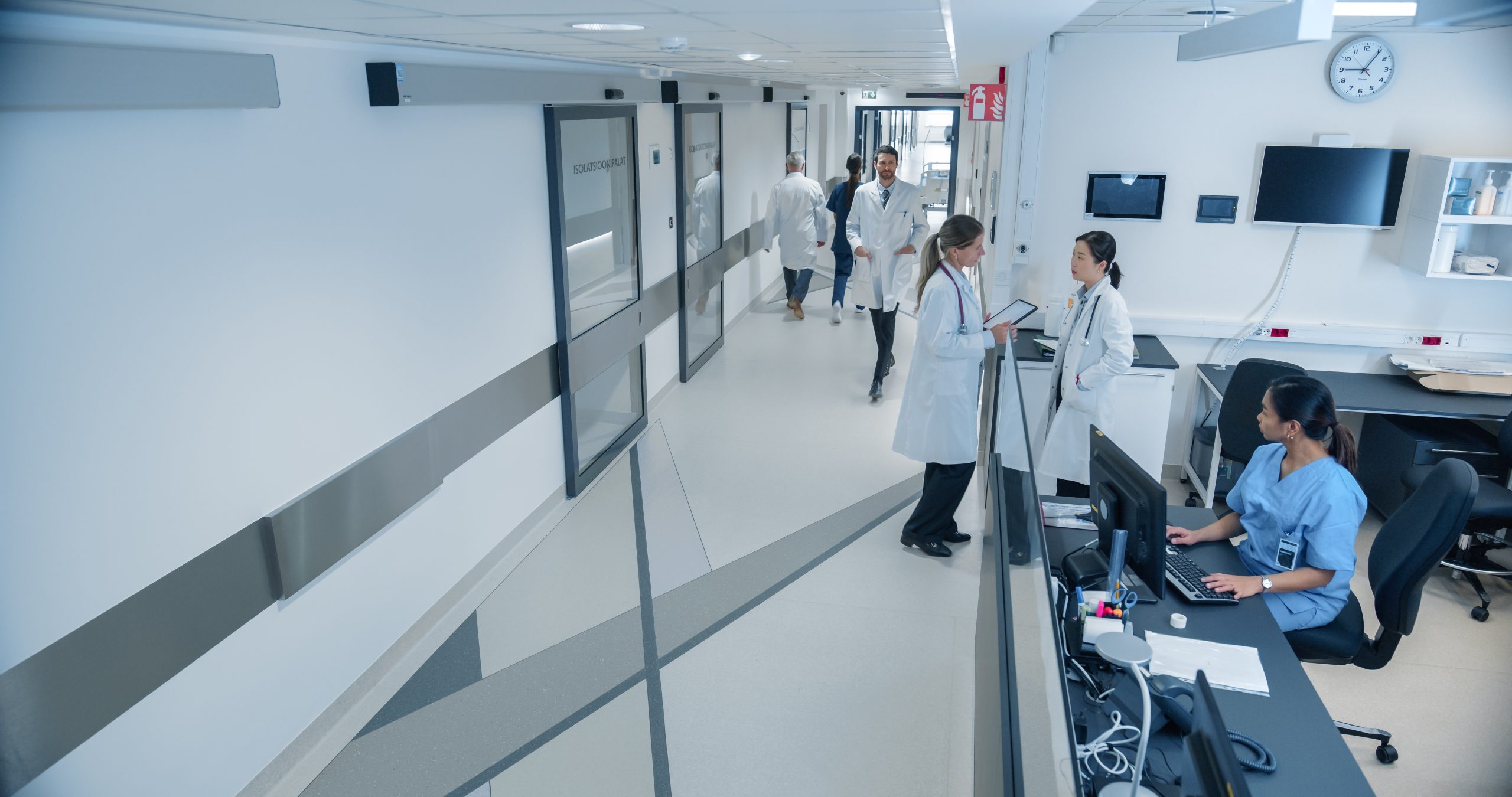High Angle CCTV Shot with a Busy Hallway with Reception Desk of a Hospital Building, Diverse Female and Male Staff Members Walking, Working. Professional Nurses, Doctors and Personnel at Work